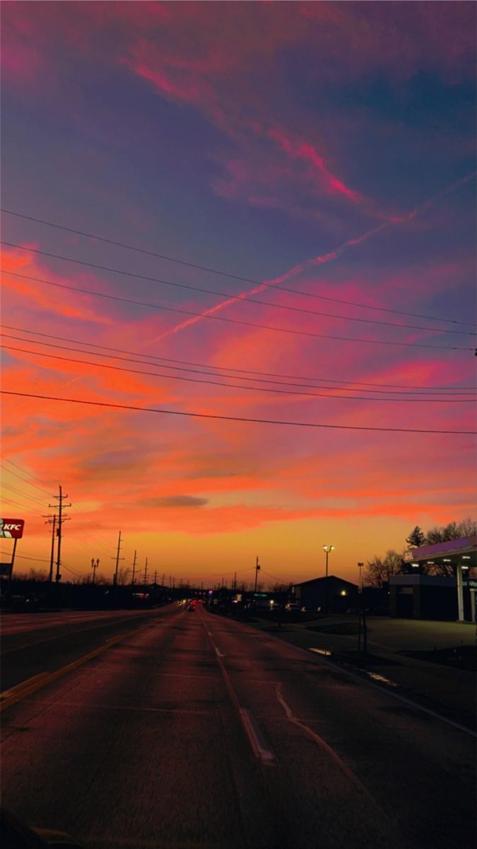 the sun is setting over an empty road with power lines in the distance and telephone poles on either side