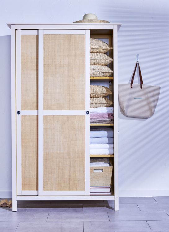 a white cabinet with some baskets in it and a bag hanging on the wall next to it