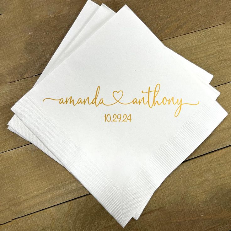 three personalized napkins with gold ink on them sitting on a wooden table top