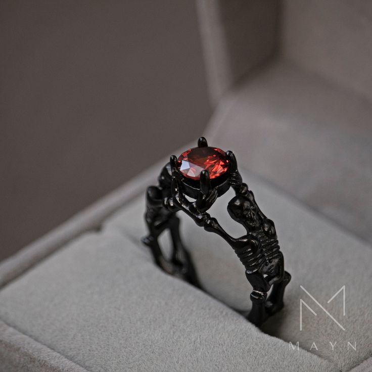 a black ring with a red stone in it's center sits inside a box