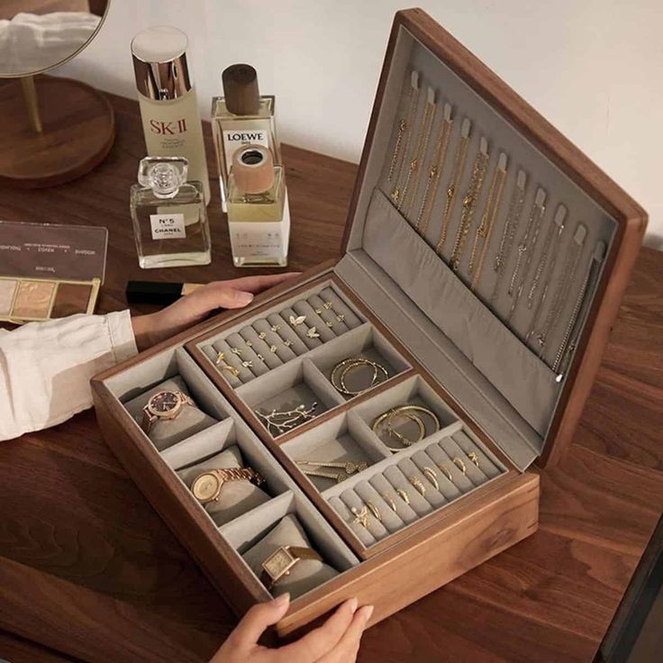 a person holding an open wooden box with jewelry in it on a table next to other items