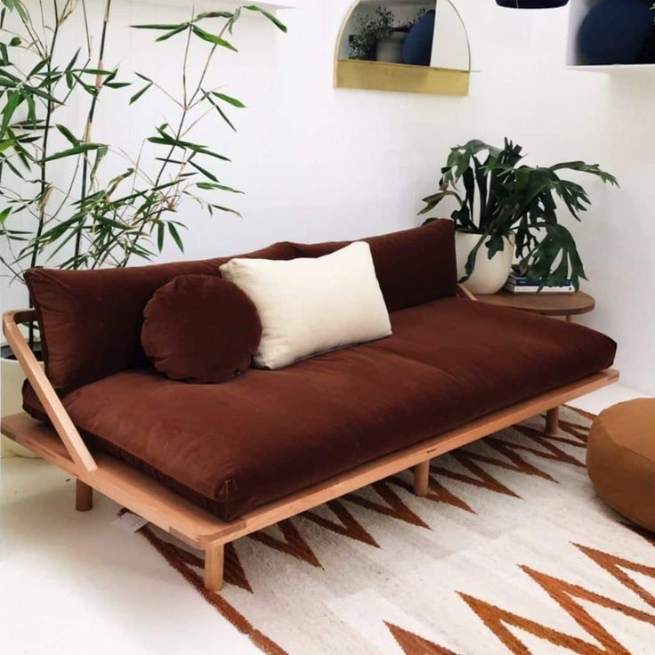 a brown futon couch sitting on top of a rug next to a potted plant