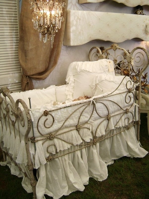 an old fashioned baby crib with white sheets and ruffled bedspread in front of a chandelier