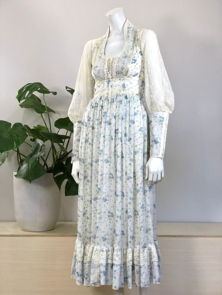 vintage lace trimmed blue & white floral print cotton voile prairie midi/maxi length dress full lace gigot sleeves w/ zippers at cuffs scoop neckline w/ lace & ribbon trimmed lace up corset bodice full gathered skirt w/ lace ruffle at hem & attached sash/tie 'Gunne Sax by Jessica San Francisco' 'Joseph Magnin' size tag 7, fits a modern x-small/small 32+ inch bust 26 inch waist 38 inch hip measurement at lining 12 1/2 inch shoulder measurement 3 1/2 inch cuff diameter 52 inch dress length 36 1/2 Spring Maxi Dress With Fitted Bodice And Long Sleeve, Spring Long Sleeve Maxi Dress With Fitted Bodice, Spring Maxi Dress With Lace Trim And Square Neck, Fitted Square Neck Maxi Dress With Lace Trim, Spring Daywear Prairie Dress With Long Sleeves, Spring Empire Waist Maxi Dress With Lace Trim, Spring Daywear Long Sleeve Prairie Dress, Spring Maxi Dress With Lace Trim And Empire Waist, Spring Long Sleeve Prairie Dress For Daywear