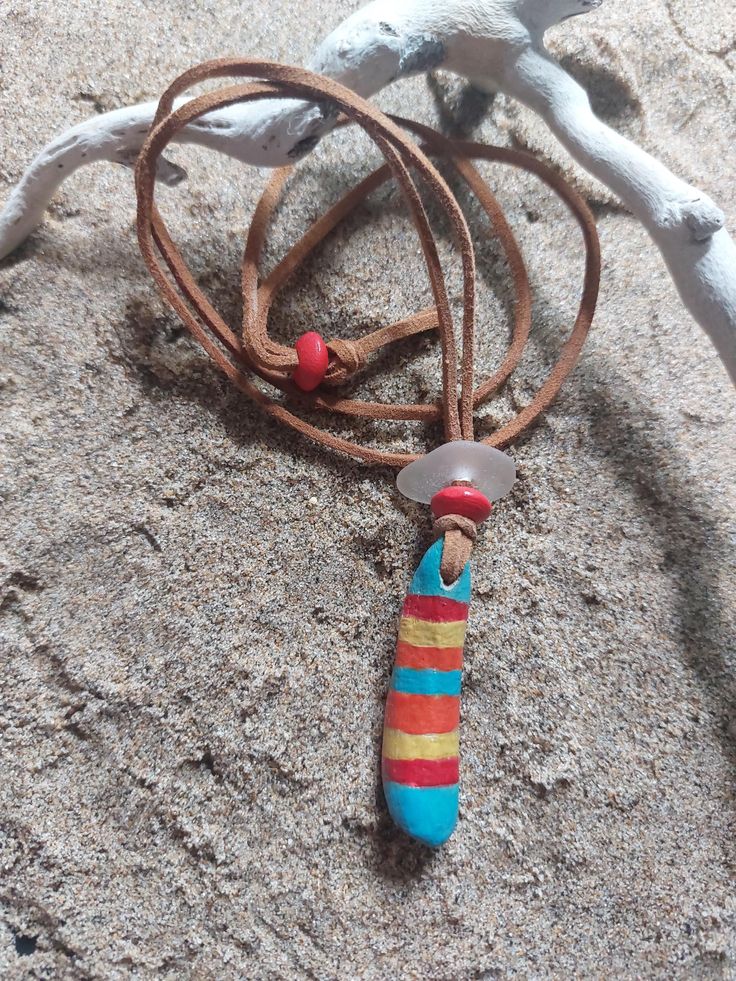 a necklace with a colorful bead hanging from it's end on the sand