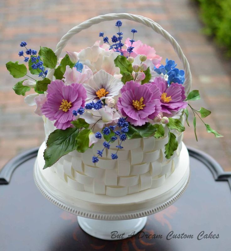 a white basket with purple and blue flowers sitting on top of a table next to a brick walkway