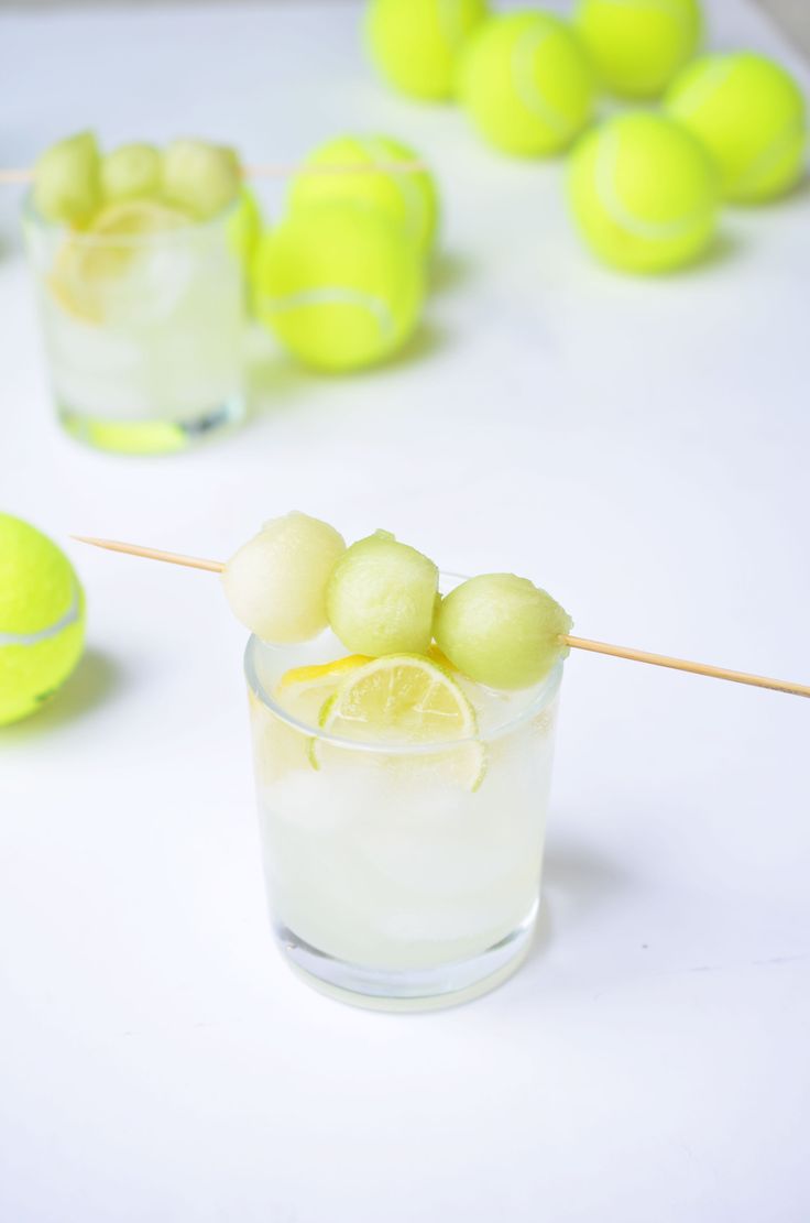 a glass filled with lemons and balls on a white table next to tennis balls