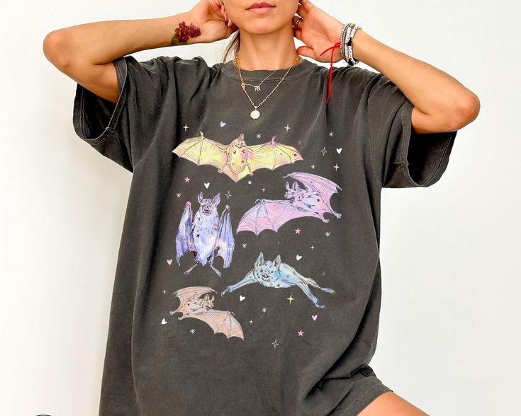 Embrace the whimsical side of Halloween with our adorable Pastel Halloween Bat Shirt! Featuring various cute pastel-colored drawings of bats, this shirt is perfect for anyone who loves a mix of spooky and girly. Ideal for fans of Whimsigoth fashion and creepy cute style, this spooky girly tee brings a touch of charm to your Halloween wardrobe. Whether you're into Goblincore or pastel goth clothes, this pink Halloween shirt is a fun and unique addition to your collection. Get ready to stand out t Halloween Short Sleeve Top For Alternative Fashion, Witchy Black Top For Costume Party, Black Witchy Tops For Costume Party, Black Witchy Top For Costume Party, Halloween Cosplay Top With Character Print, Character Print Tops For Halloween Cosplay, Fall Graphic Print Tops For Cosplay, Halloween Crew Neck Top For Alternative Fashion, Spooky Graphic Print Tops For Alternative Fashion