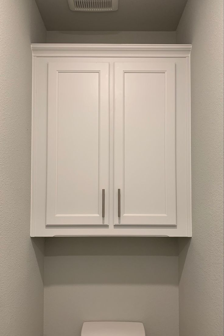 a white toilet sitting under a cabinet in a bathroom