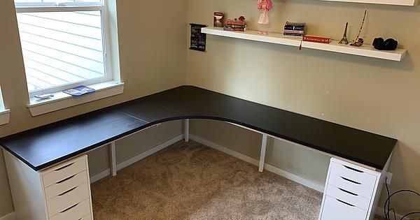 a corner desk with drawers underneath a window in a room that has carpet on the floor