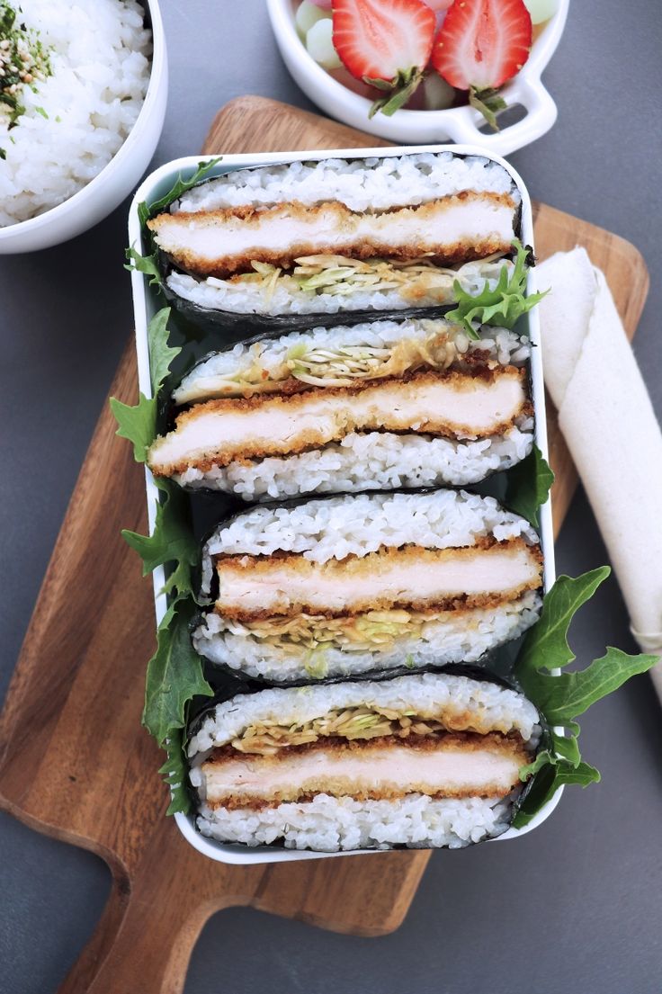 sushi in a container on a cutting board with strawberries and other food items