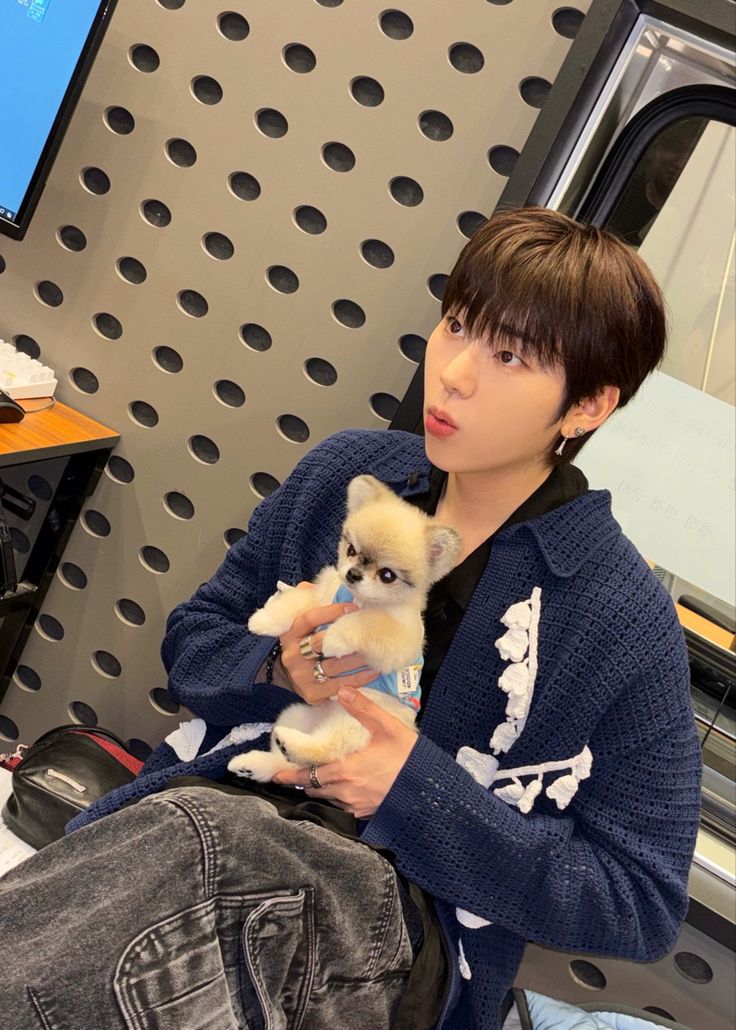 a young man holding a small dog in his lap and looking at the camera while sitting on a chair