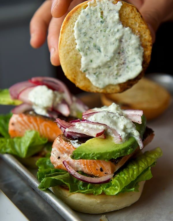 a sandwich with salmon, lettuce and onions being held up by someone's hand