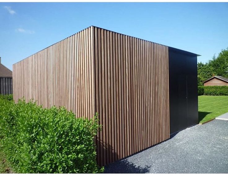 a wooden building sitting on the side of a road next to a lush green field