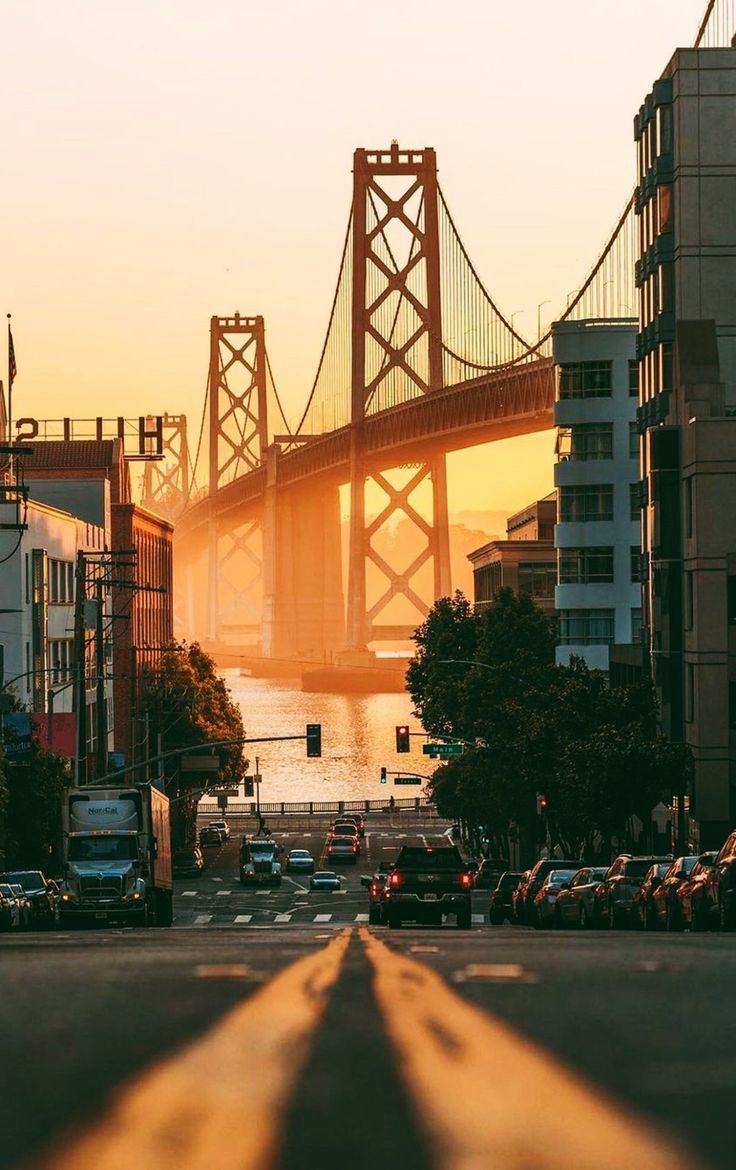 the sun is setting behind a bridge and cars are parked on the side of the road