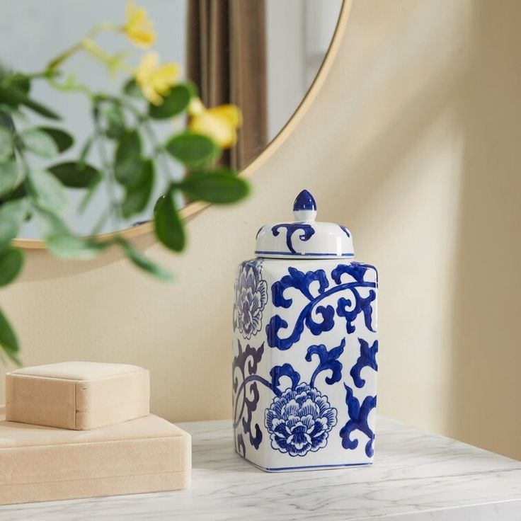 a blue and white jar sitting on top of a table next to a mirror with yellow flowers