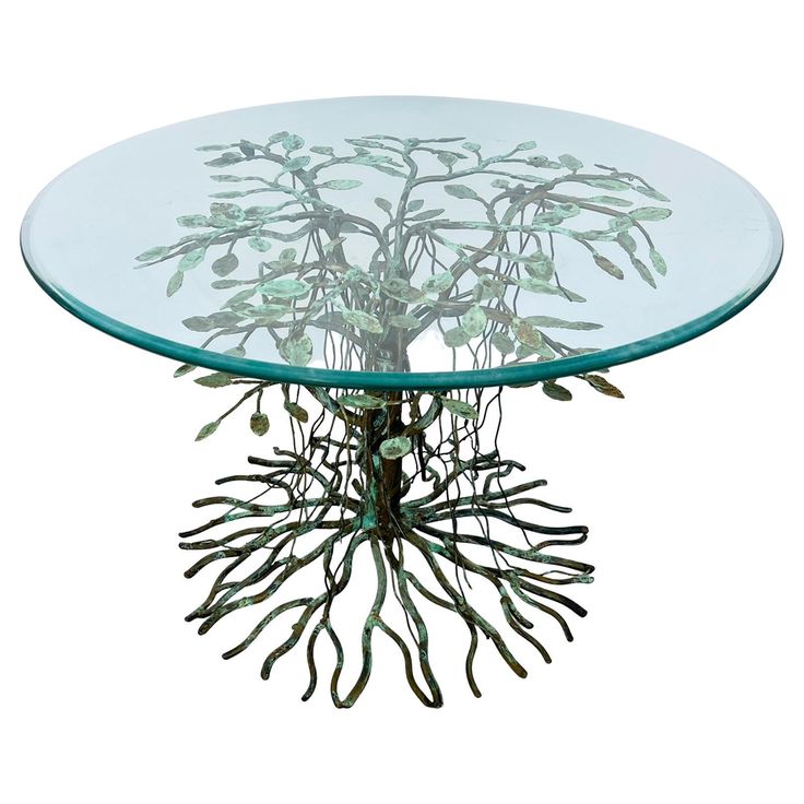 a glass table with metal branches and leaves on it's base, against a white background