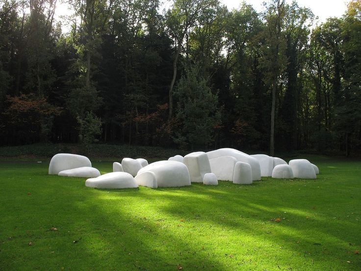 a group of white sculptures sitting on top of a lush green field next to trees