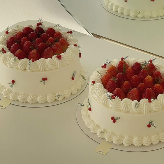 two cakes with white frosting and strawberries on top