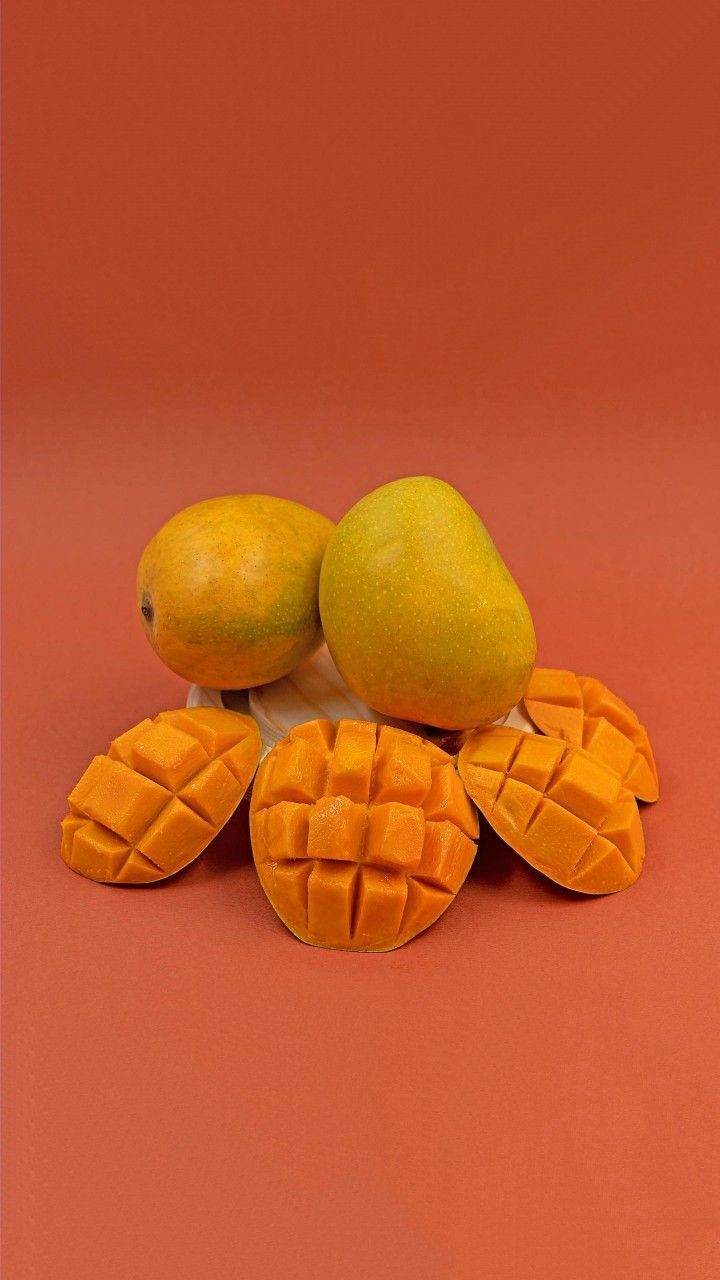 three mangoes and two oranges on a red background with one cut in half