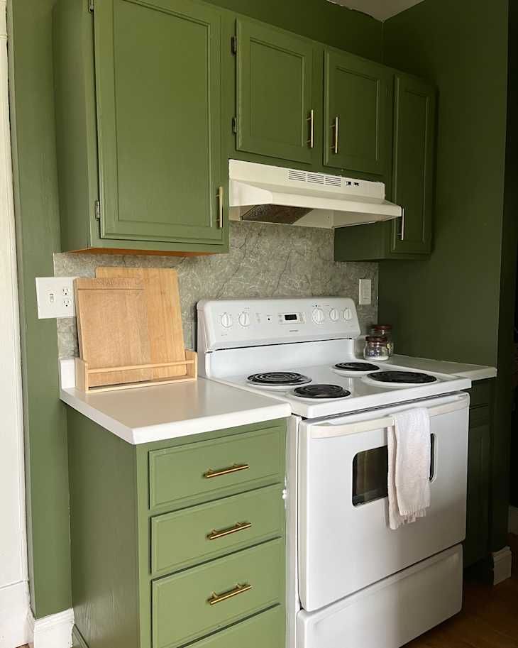 a white stove top oven sitting inside of a kitchen next to green cupboards and cabinets