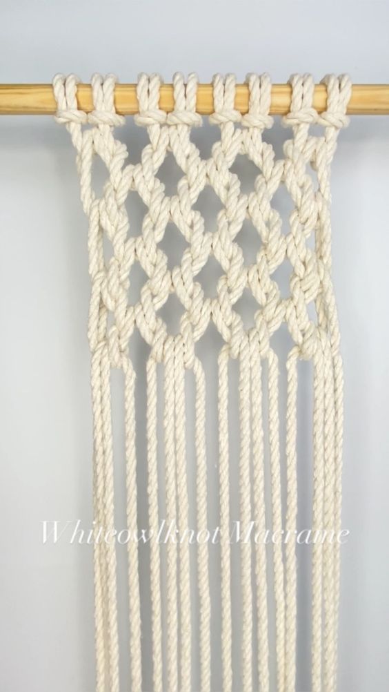 a white macrame hanging on a wall with a wooden stick in front of it