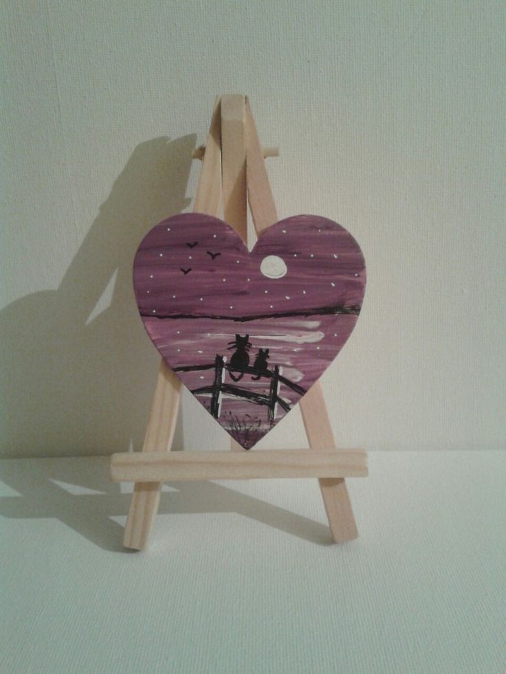 a wooden easel with a heart shaped painting on it's back and two people standing in the background