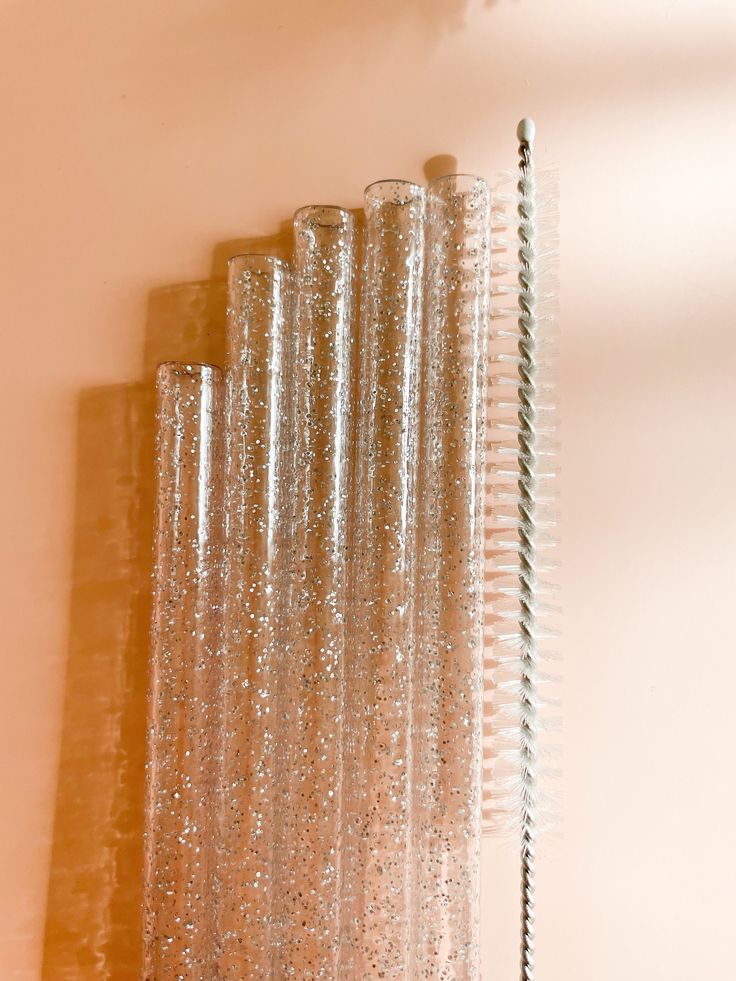 three clear glass vases sitting next to each other on a white wall behind a curtain