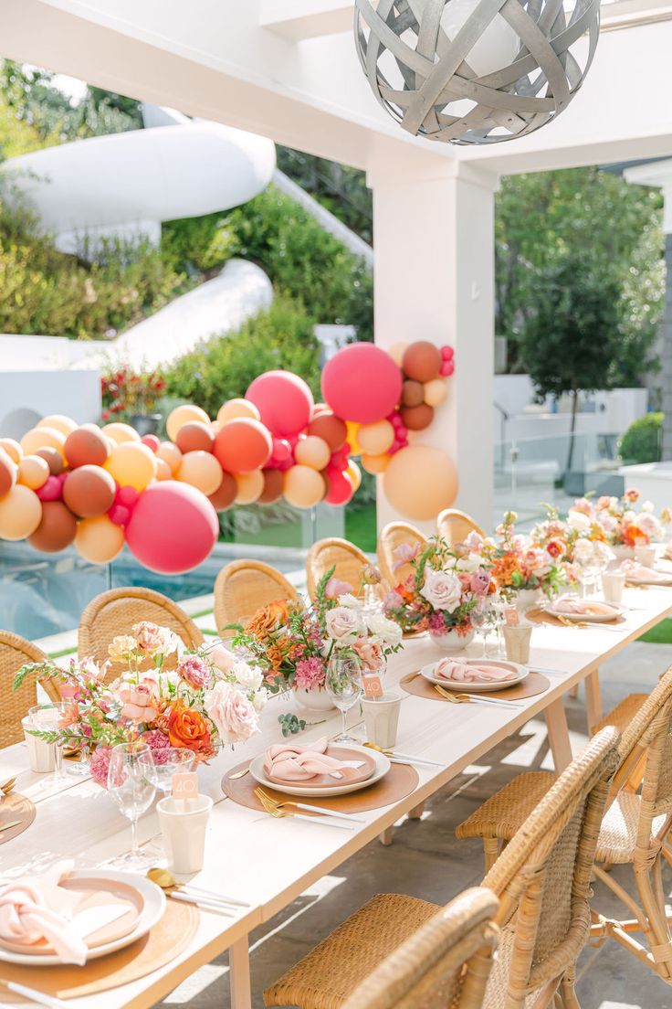 a table set up for a party with balloons in the air and flowers on it