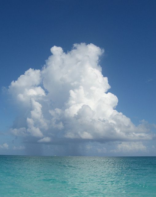 a large cloud is floating in the sky over the blue water on a sunny day