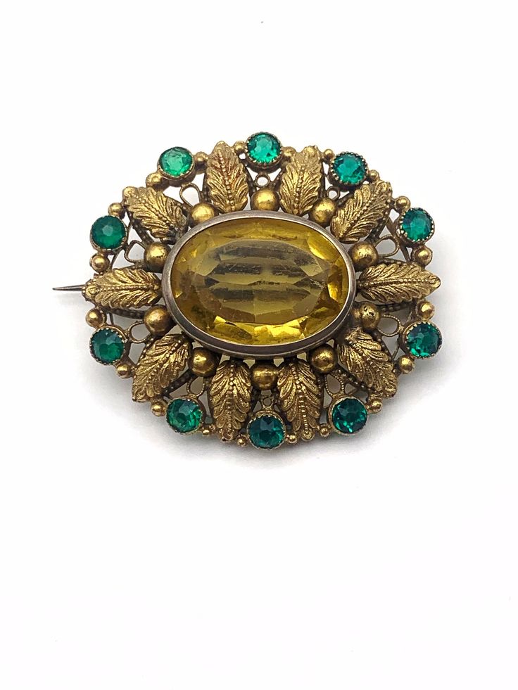 "This brooch is a lovely example of an circa 1890s/1900s Victorian pin design. It is a Victorian metalwork masterpiece with a beautiful rhinestone setting. A large impressive piece, that look amazing worn! This gold filled metal design is richly detailed with fern leaves frame, metal bead work, open work design of the period graceful by green crystals that delineate the outer edge  The 25mmx18mm large topaz, faceted glass rhinestone is in a high bezel, open back setting. Also the 5mm green stone Ornate Jeweled Gold Brooches, Ornate Gold Jeweled Brooches, Ornate Gold Brooches For Vintage Events, Antique Gold Brooches For Vintage Events, Victorian Jeweled Wedding Brooches, Victorian Green Collectible Brooches, Victorian Jeweled Gold Brooches, Antique Jeweled Brooch For Wedding, Art Deco Green Brooches For Wedding