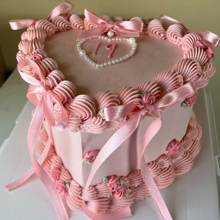 a heart shaped cake with pink icing and bows on it's edges, decorated with pearls