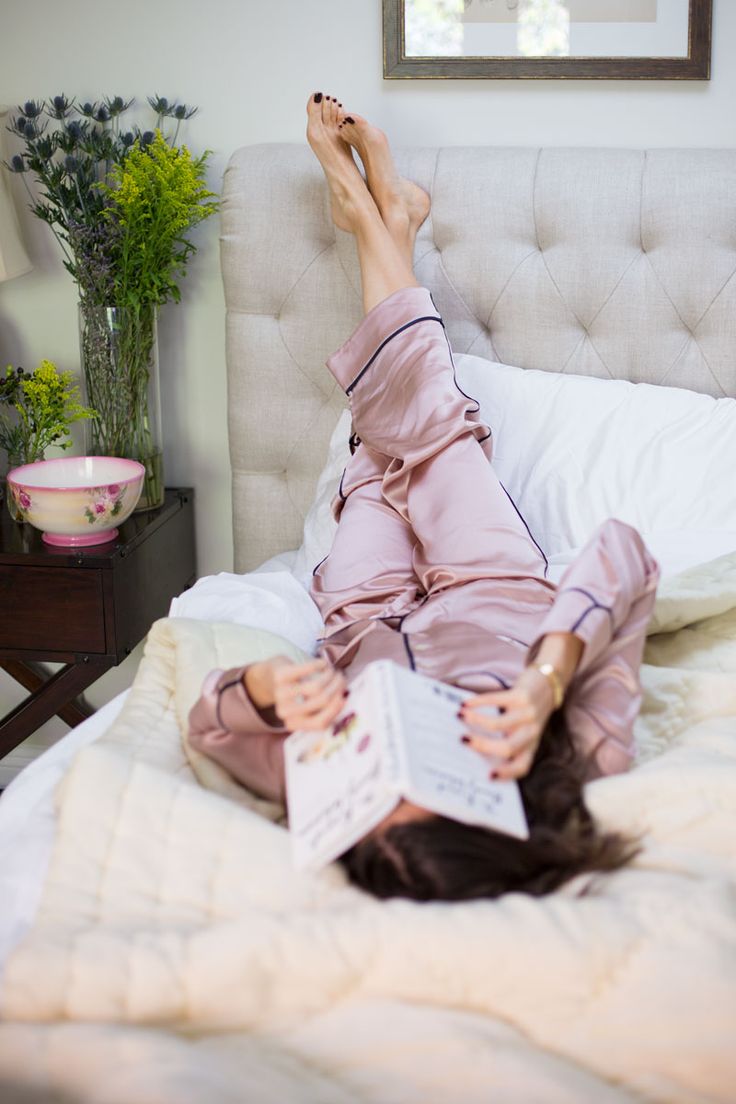 a woman laying on top of a bed with her feet up and reading a book