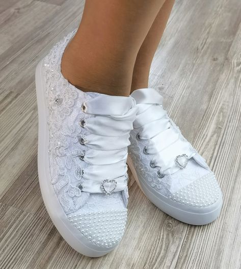 a woman's white sneakers with lace and bows on the side, sitting on a wooden floor