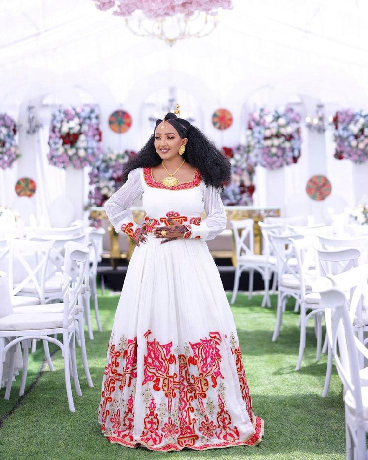 a woman in a white and red dress standing next to tables with flowers on them