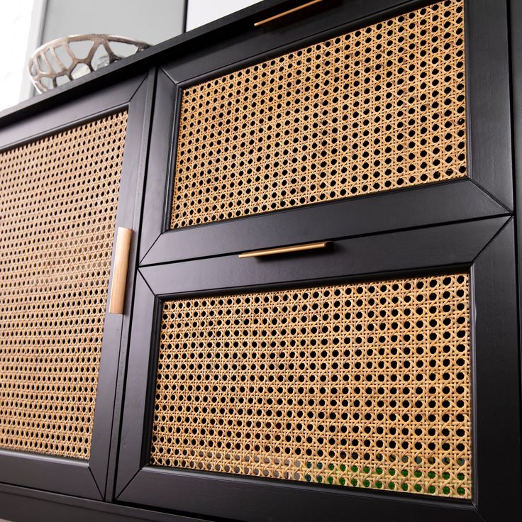 a black cabinet with some gold handles on the front and side panels that are made out of rattan