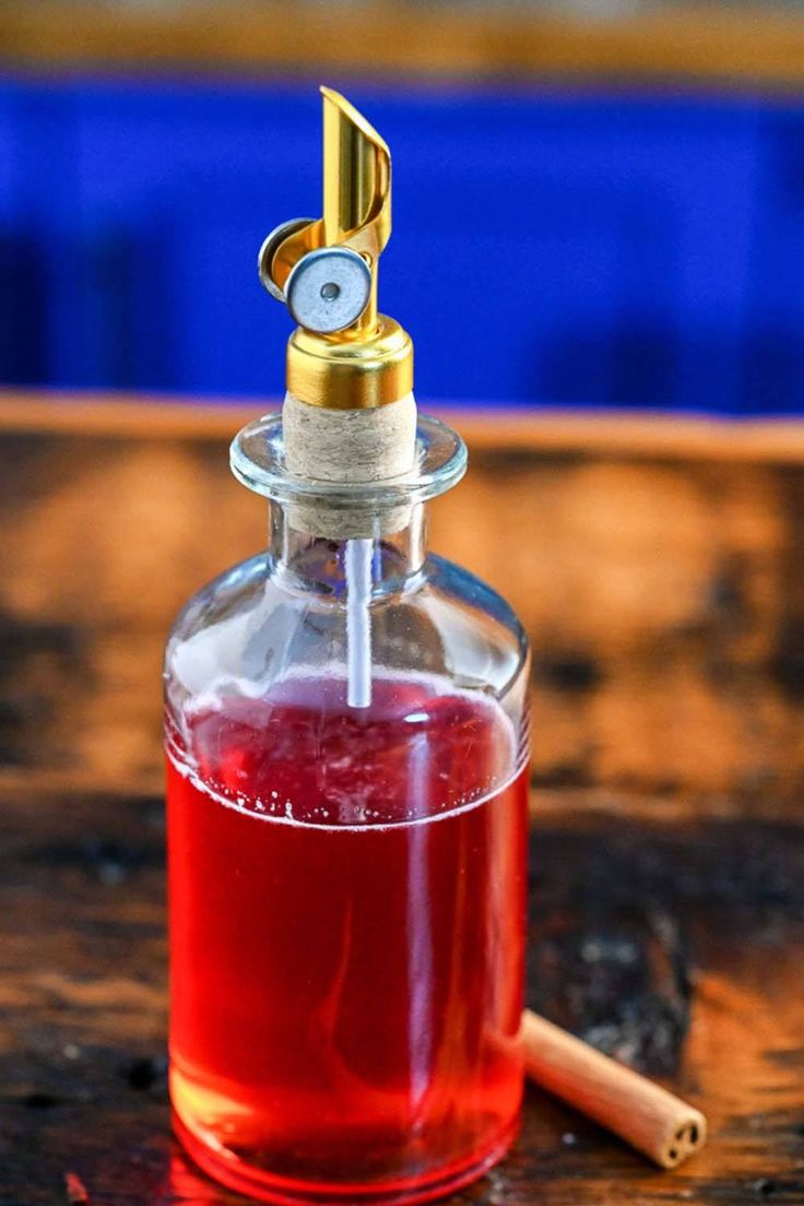 a glass bottle filled with liquid sitting on top of a wooden table next to a cinnamon stick