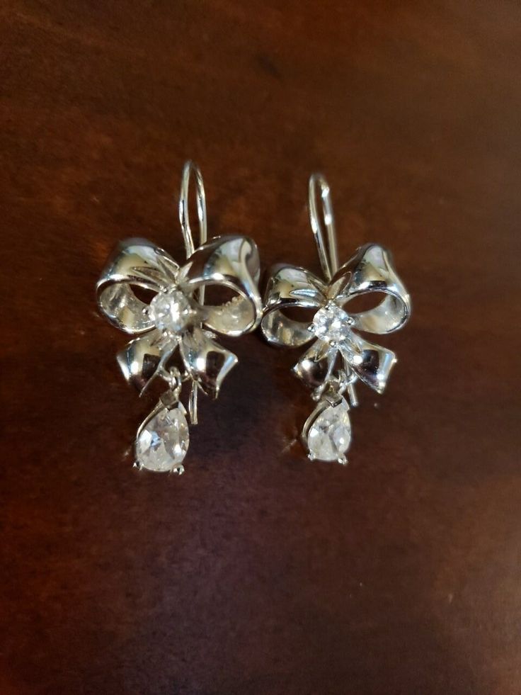 These are SO SO PRETTY! Beautiful Bows, centered with a 4mm round CZ, and dangling another 8x5mm pear shape. Sterling Silver, layered with Platinum, and featuring Cubic Zirconia stones; this is the Epiphany Line by Diamonique The closure is also one of my favorites - an elongated earwire that is secured by a little "shepherd's hook" on the bottom. Easy to do, nothing to drop or lose, secure & comfortable 😊 Measure 1.25" long, 5/8" wide Hallmarked SW 925 CZ CHINA Contact me with any questions Elegant Diamond Crystal Earrings For Gift, Silver Crystal Chandelier Earrings For Anniversary, Cubic Zirconia Chandelier Earrings With Diamond Accents As Gift, Chandelier Earrings With Diamond Accents As Gift, Cubic Zirconia Chandelier Earrings With Diamond Accents, Gift Chandelier Earrings With Diamond Accents, Gift Chandelier Drop Earrings With Sparkling Stones, Sparkling Stone Chandelier Drop Earrings As A Gift, Anniversary Crystal Diamond Drop Earrings