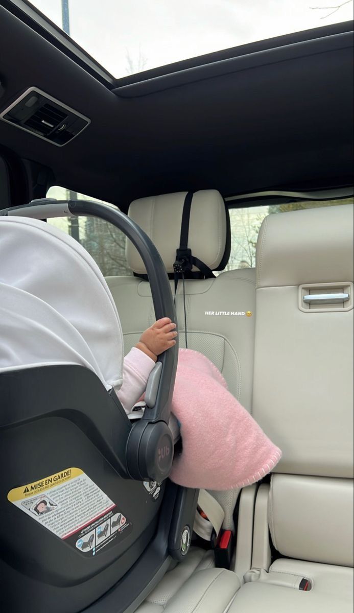 a baby sitting in a car seat with a pink blanket on it's head