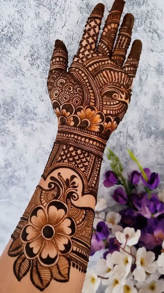 a woman's hand with henna tattoos on it and flowers in the background