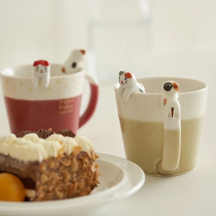 two cats figurines sitting on top of a plate next to a piece of cake