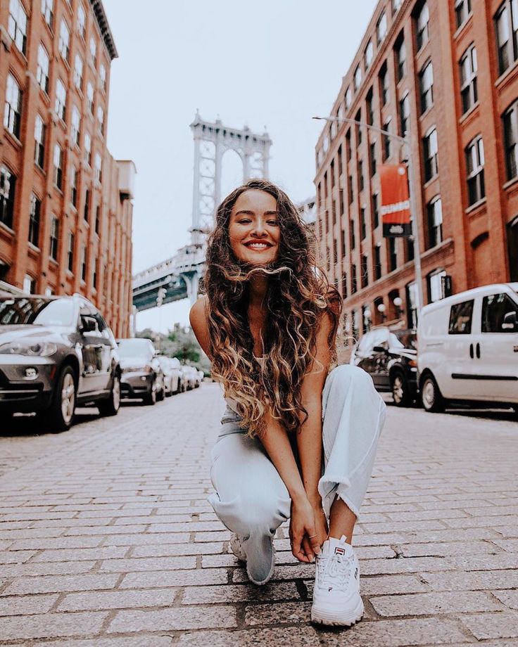 a woman sitting on the ground in front of some tall buildings smiling at the camera