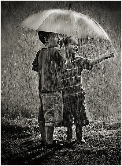 two children standing in the rain with an umbrella