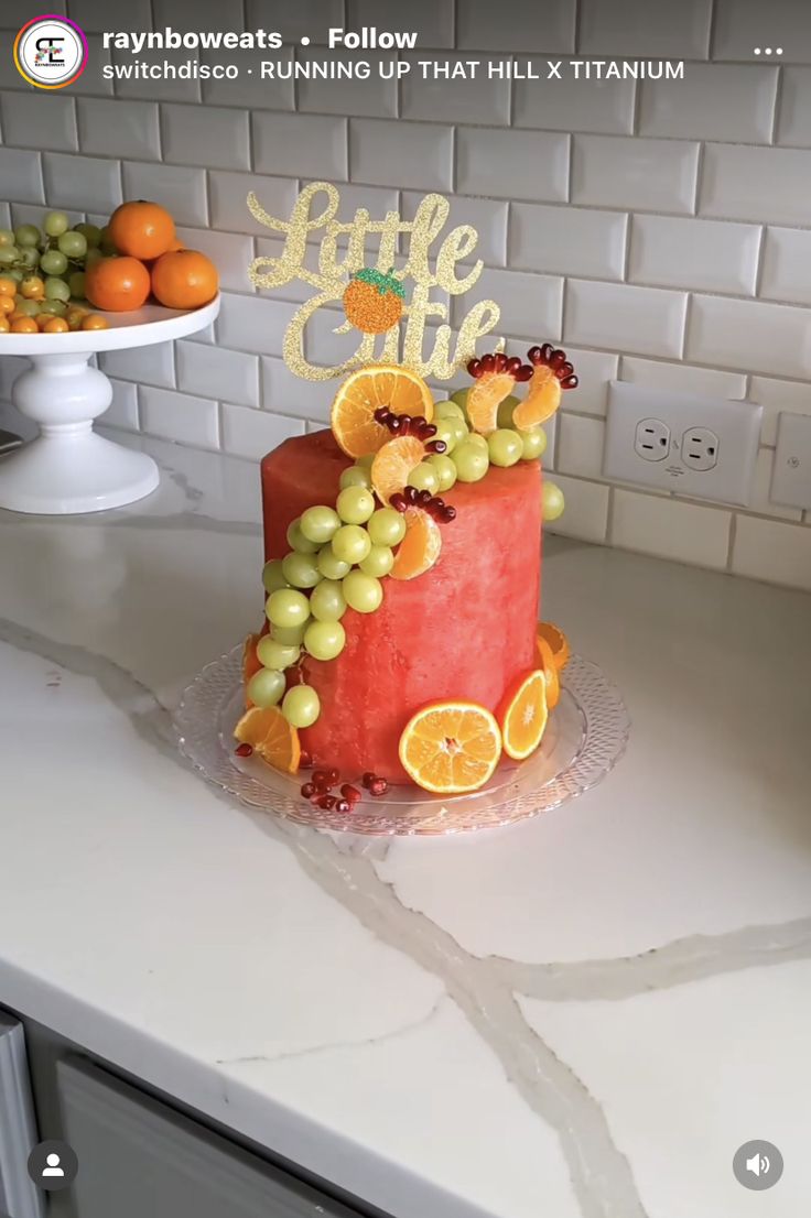 a cake decorated with oranges and grapes on top of a counter next to other fruits