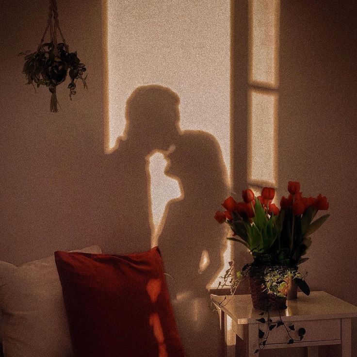 the shadow of a person standing in front of a window next to a table with flowers