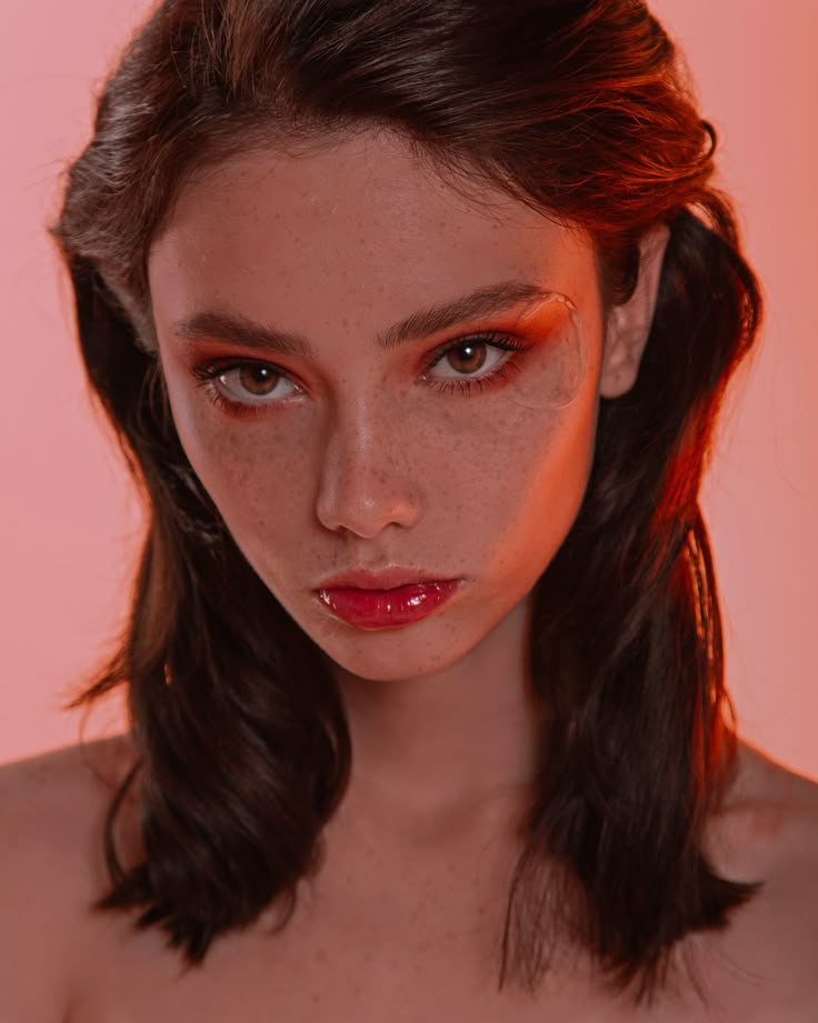 a woman with freckled hair and makeup looks at the camera while wearing red lipstick