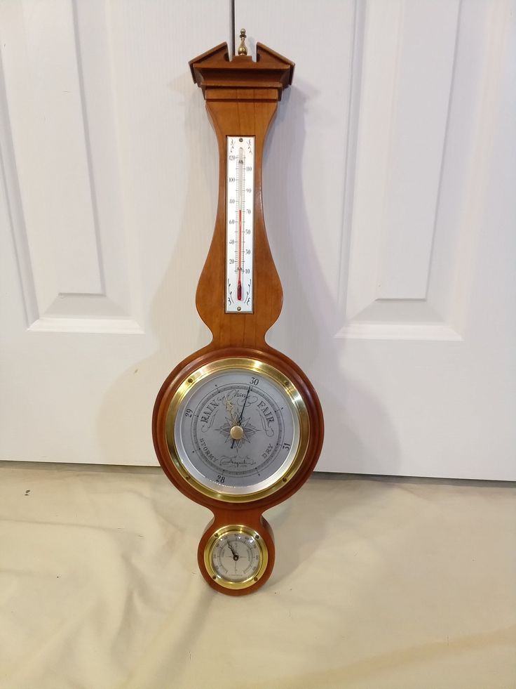 an old wooden clock hanging from the side of a white door with a barometer attached to it