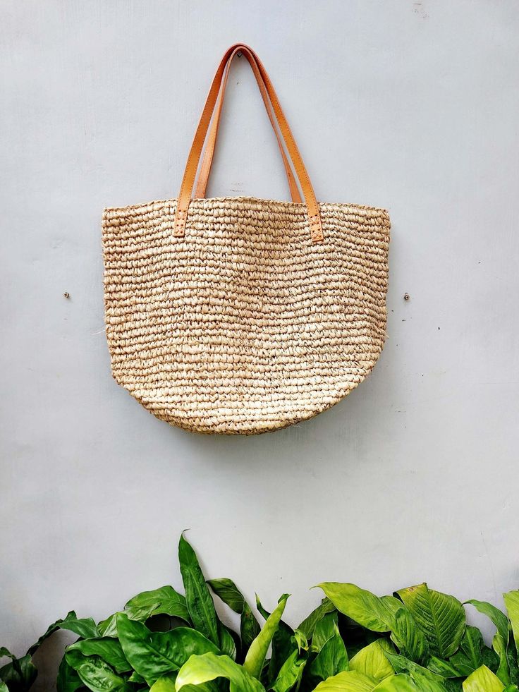 a straw bag hanging from the side of a wall next to green plants and potted plants