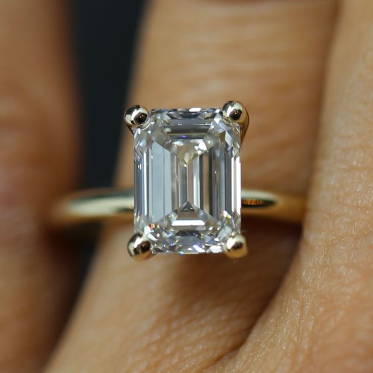 a woman's hand with a diamond ring on her left side and an emerald stone in the middle