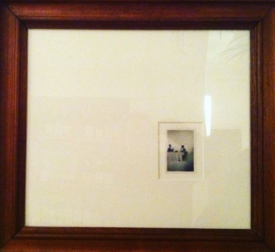 an old framed photograph hanging on the wall in front of a wooden frame with a white background